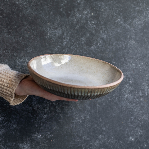Hand holding a Progress Stu Bowl, displaying the White Chamois interior glaze and etched exterior texture. The Shallow bowl is used for pasta and stews