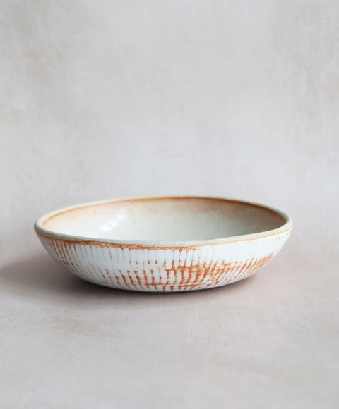 Side view of a Workshop Stu Bowl, showcasing its creamy glaze and the exterior texture. The shallow bowl is great for stus and pastas