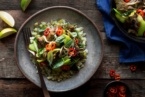 Progress Pasta Bowl glazed in Moonshadow, containing meat and vegetables. Bowl is displayed with a fork and limes on a rustic wooden table