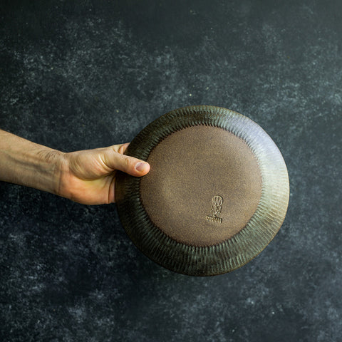 Hand holding a Progress Stu Bowl, displaying the unglazed bottom and etched texture, glazed in Moonshadow