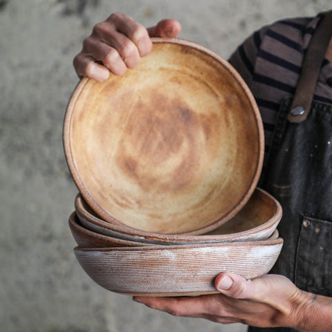 MaryMar holding a stack of Sierra Stu Bowls, showcasing the interior glaze of the top bowl in Brown Leather Matte. These shallow bowls are perfect for stews and pasta
