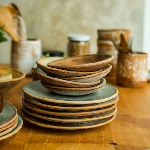 Stack of Sierra Salad Plates and Dessert Bowls on a wooden table with more MMclay Sierra pieces in the background