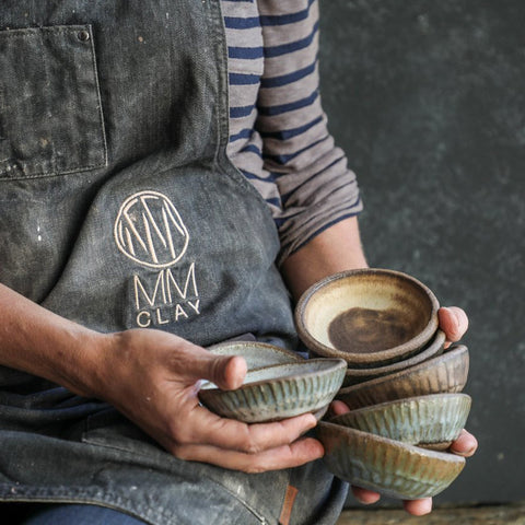 Someone wearing an MMclay apron, holding a handful of Progress Ramekins