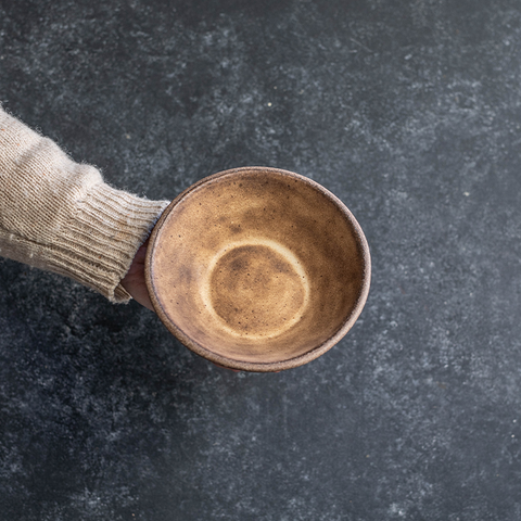 Hand displaying the interior of a Progress Small Soup Bowl glazed in Brown Leather Matte. 