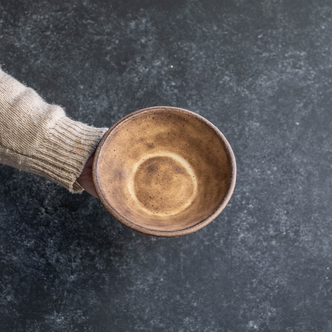 Hand displaying the interior of a Progress Small Soup Bowl glazed in Brown Leather Matte.