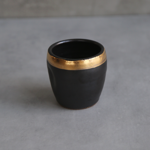 Black ceramic cup with gold rim on a gray background
