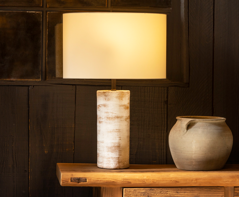 Handmade Rustic Table Lamp with a warm glow. It sits on a wooden counter next to a rustic vase.