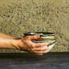 Cupped hand holding stack of three Inkblot cereal bowls in front of a natural stone wall