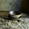 Progress Cereal Bowl glazed in Eelskin, displayed with a Cafe Plate, in dramatic lighting on a rocky textured surface