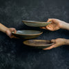 Hand passing a variety of Progress Pasta Bowls, glazed in Moonshadow, White Chamois, and Brown Tan Matte