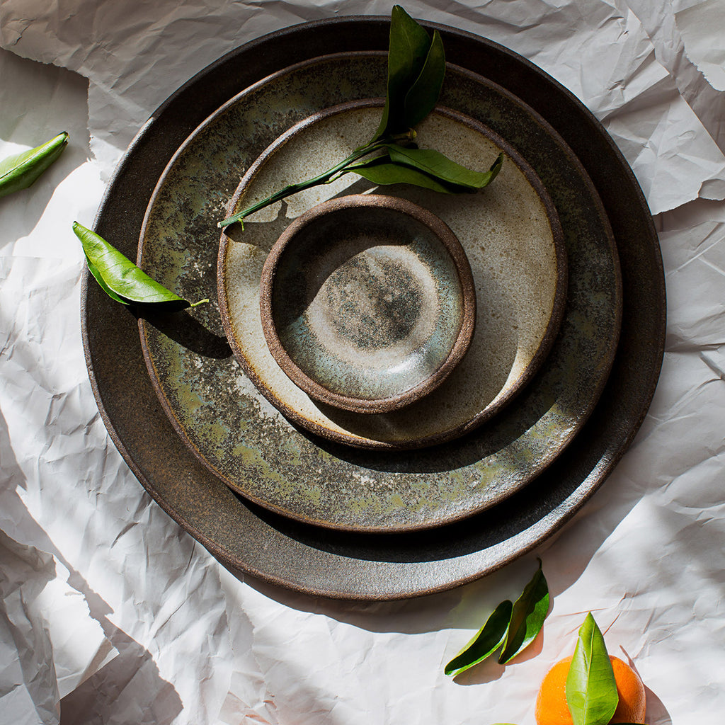 Stack of Progress Plates glazed in Moonshadow photographed in dramatic lighting, adorned with a clementine and its leaves