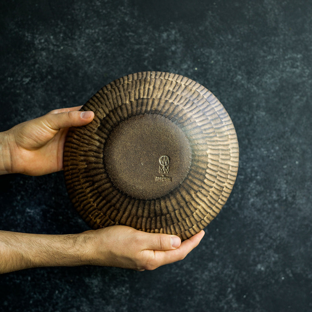 Hand displaying the bottom of a Progress Serving Bowl, highlighting the hand etched texture glazed in Brown Leather Matte