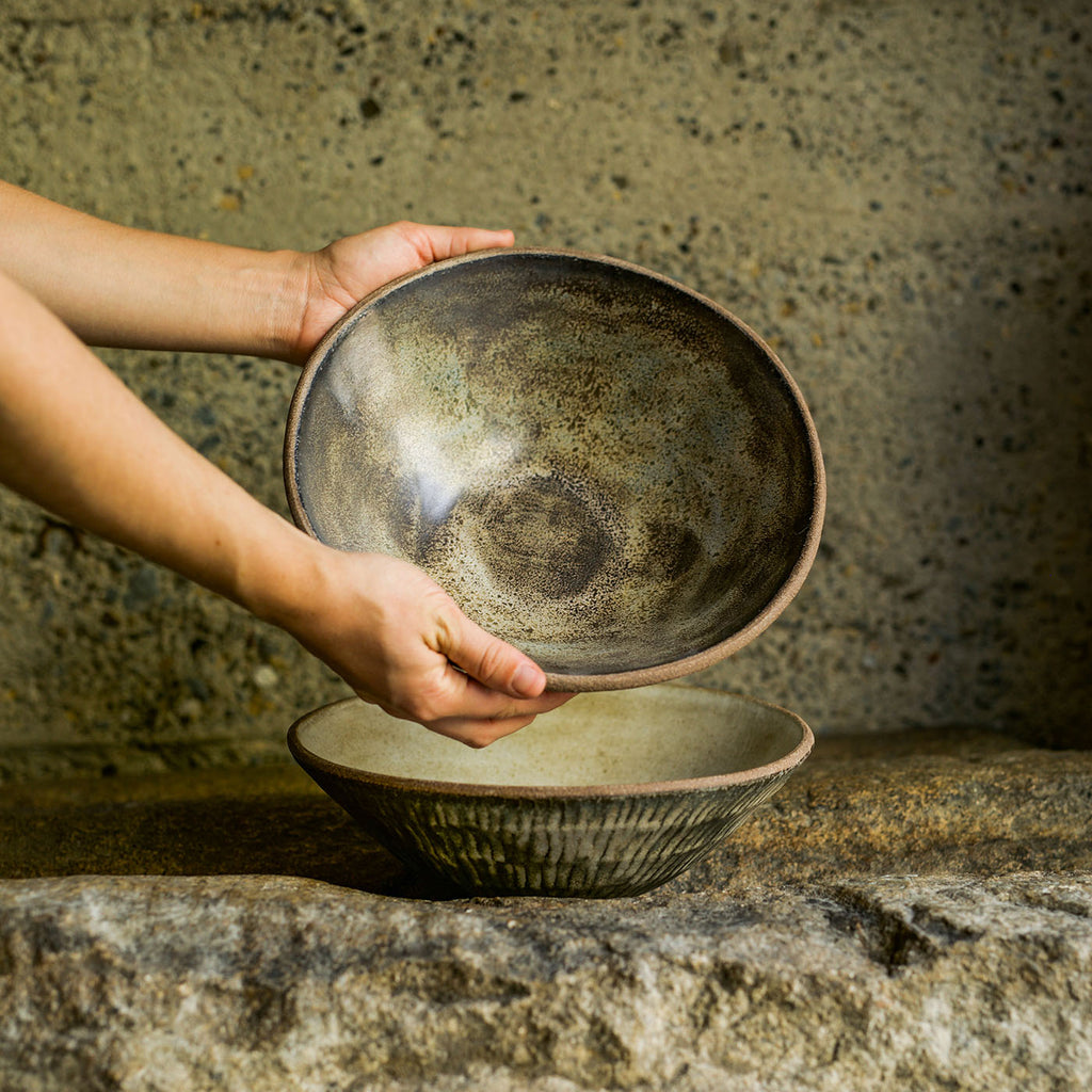 Two Progress Serving Bowls displayed in dramatic lighting on a rocky earthy surface