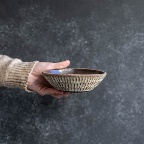 Hand displaying a Progress Small Soup Bowl glazed in Eelskin. The hand etched texture on the exterior is glazed in White Chamois