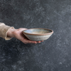 Hand displaying a Progress Small Soup Bowl glazed in Moonshadow. The hand etched texture on the exterior is glazed in White Chamois